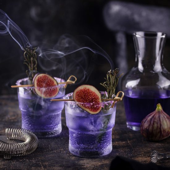 Purple fig cocktail or mocktail in glass on green olive background